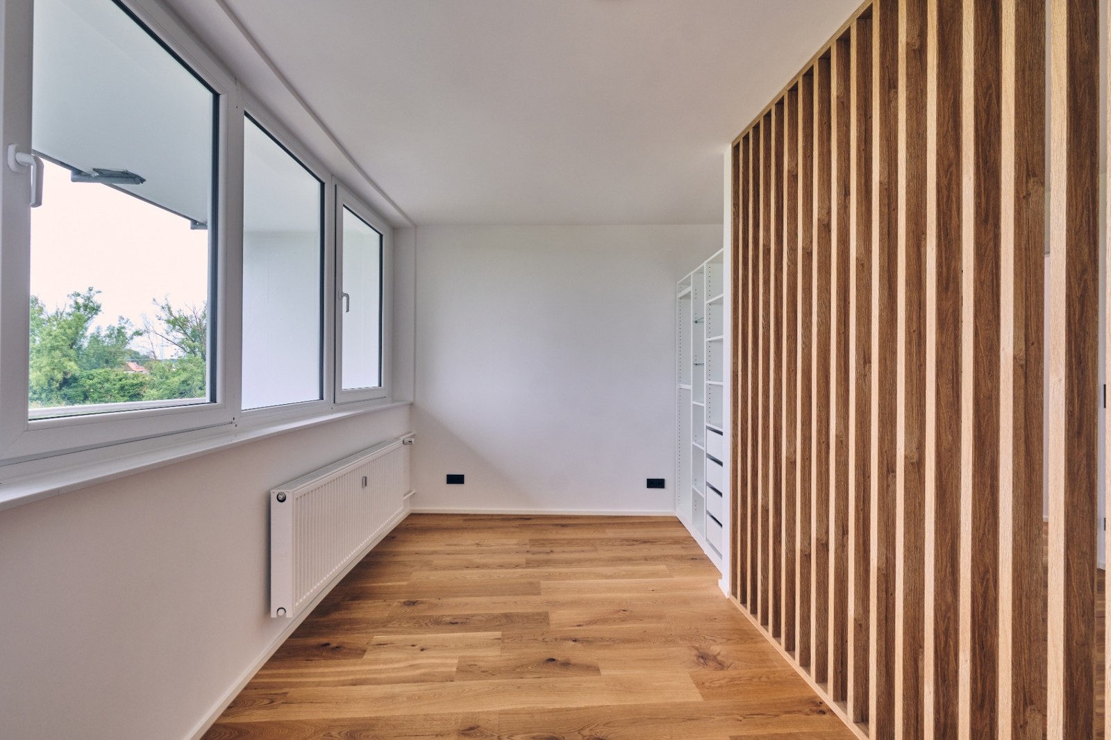 Lichtdurchfluteter Raum mit Holzlamellen-Wand, Einbauschrank und Eichendielen